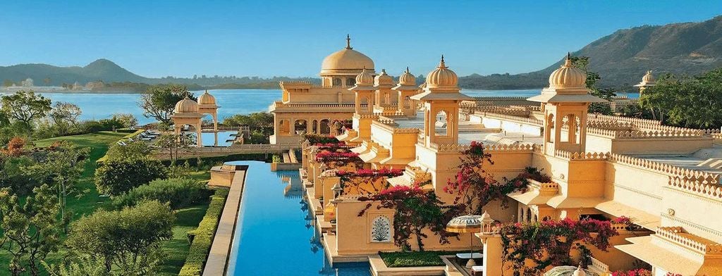 Opulent domed palace-hotel with cream facades and intricate archways reflected in vast pools, surrounded by manicured gardens at sunset