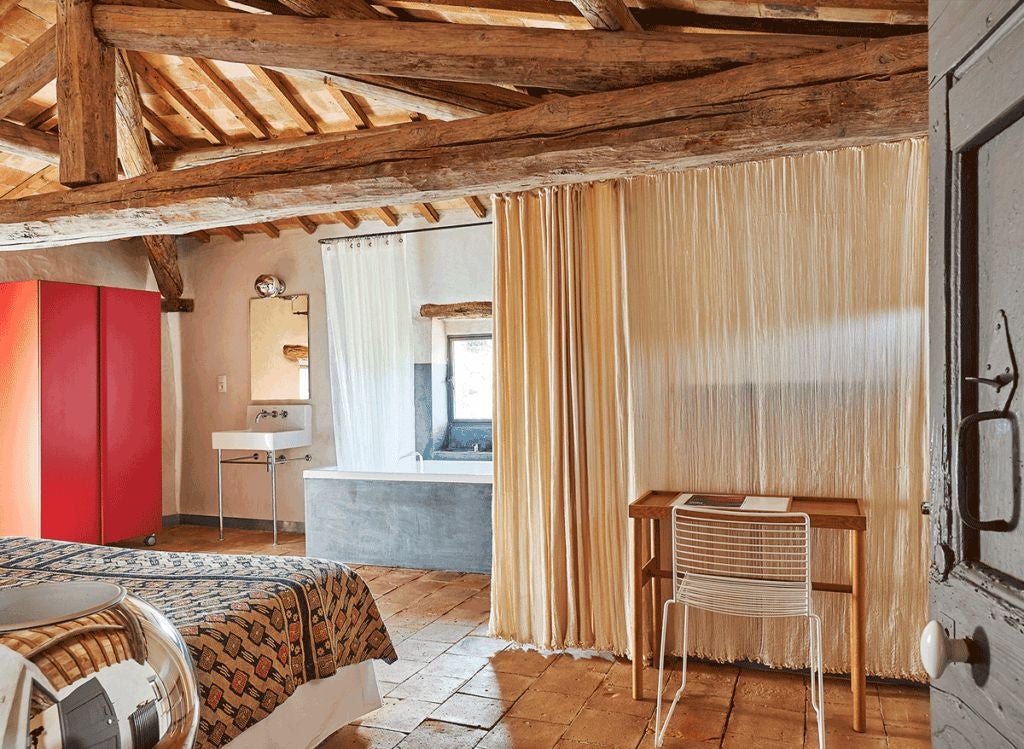 Elegant stone-walled hotel room with rustic wooden furniture, soft linens, and large windows overlooking lavender fields in southern France