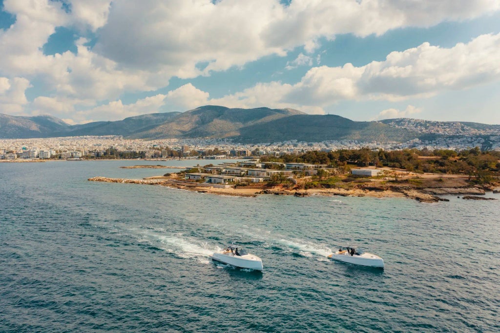 Luxurious white minimalist hotel with infinity pool overlooking the Aegean Sea, nestled among rocky coastline and Mediterranean landscape in Greece