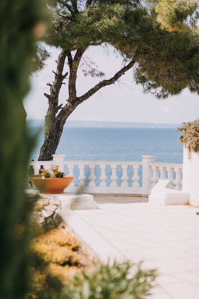 Luxurious white villa with minimalist design, featuring expansive sea view, private infinity pool, and elegant coastal Greek architecture at sunset