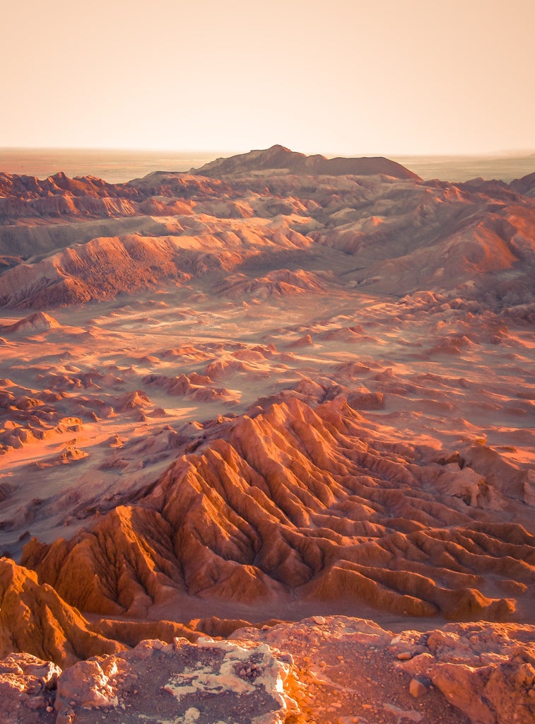 Sunset illuminates luxury glamping domes nestled among red rock formations in Chile's Atacama Desert, stars visible above