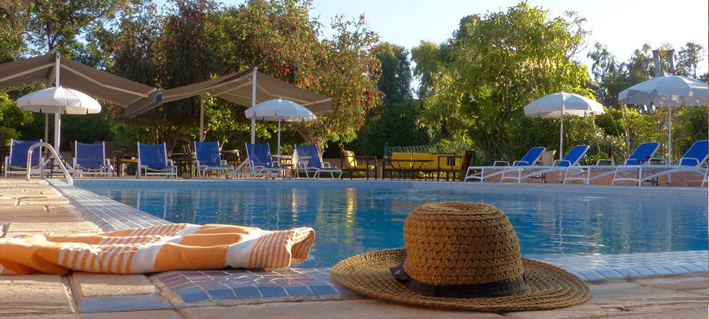 Elegant Moroccan boutique hotel with terracotta walls surrounded by lush orange grove gardens, white archways, and a tranquil pool