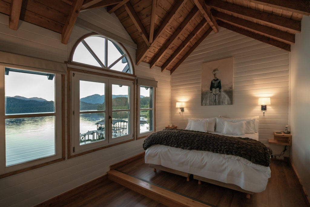 Luxurious lakeside hotel room with floor-to-ceiling windows, panoramic Patagonian landscape, elegant minimalist design, warm wood tones, and plush furnishings