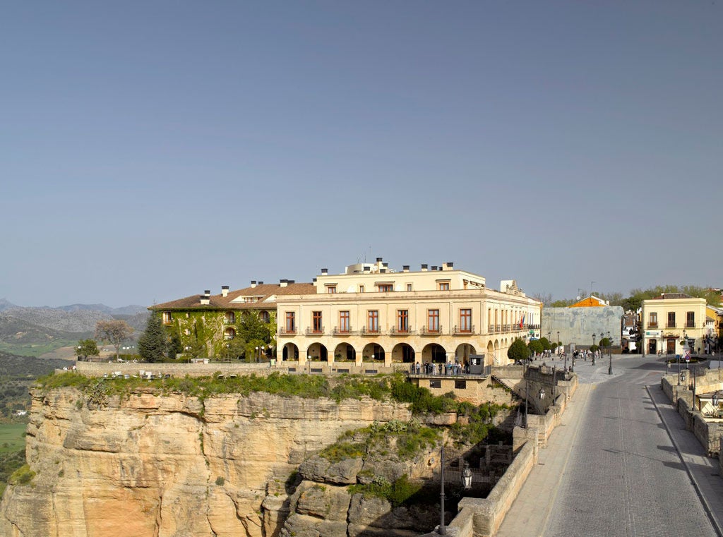 Historic Spanish Parador hotel with stone archways and ornate balconies, nestled against mountains, featuring manicured gardens and fountain