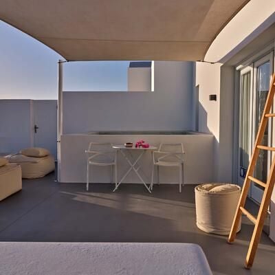 Sunlit white-washed luxury suite with panoramic Aegean Sea view, minimalist design, fresh herb accents, and elegant blue-trimmed Santorini architectural details