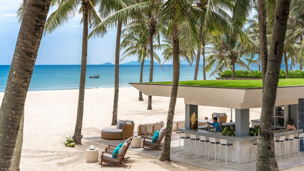 Luxurious infinity pool overlooking pristine beach at Nam Hai resort, with palm trees and traditional Vietnamese architecture at sunset