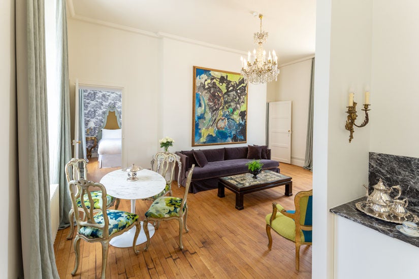 Elegant French château hotel room with two king beds, ornate crown molding, crystal chandelier, and floor-to-ceiling windows overlooking courtyard