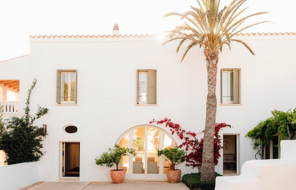 Elegant whitewashed Spanish hotel room with minimalist design, soft neutral tones, crisp linens, and panoramic countryside view through large windows at Torralbenc.