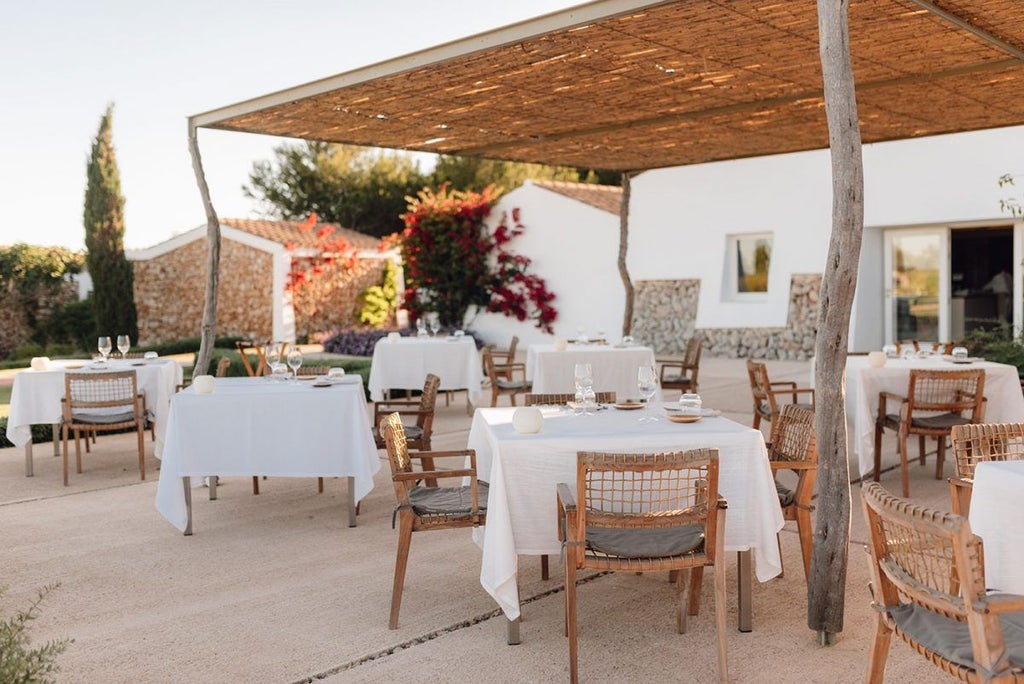 Luxurious whitewashed Menorcan farmhouse hotel with stone walls, surrounded by lavender fields and rustic Mediterranean landscape at sunset