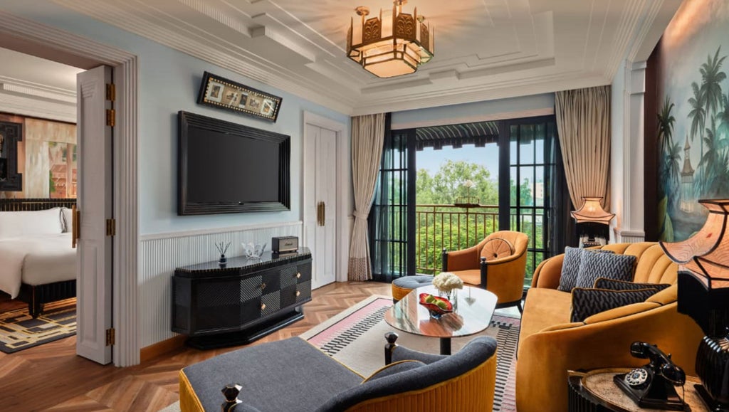 Opulent colonial-style suite with art deco touches, featuring king bed, crystal chandelier, ornate golden decor and city views of Hanoi