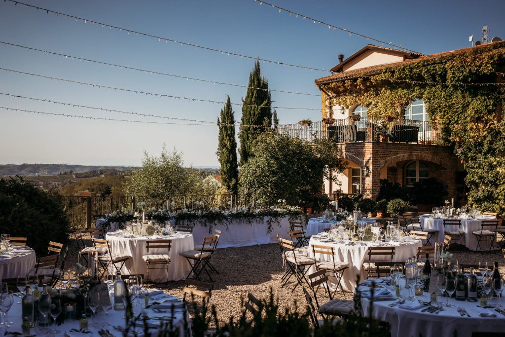 Elegant stone villa hotel with terracotta roofs nestled in Tuscan countryside, surrounded by lush cypress trees and rolling green hills at sunset