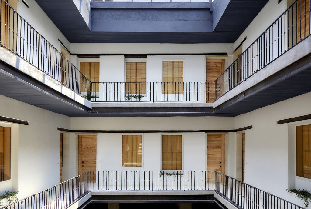 Elegant minimalist boutique hotel with terracotta-colored walls, modern Mexican design, sunlit courtyard with geometric arches and lush greenery