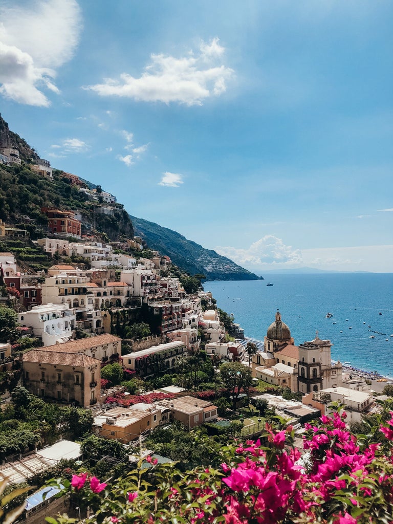 Winding coastal roads hug dramatic cliffs overlooking turquoise Mediterranean waters, with colorful houses perched along Amalfi's hillside