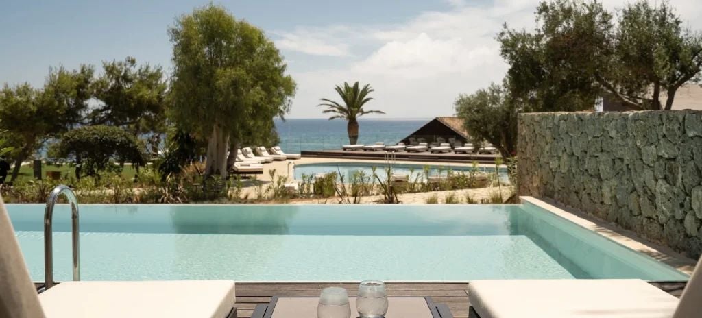 Elegant Patio Junior Suite with white-washed Mediterranean aesthetic, private balcony overlooking lush greenery at Domes of Corfu resort in Greece