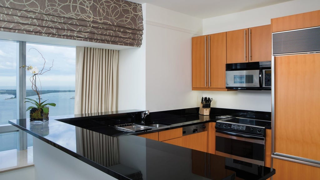 Spacious Two-Bedroom Residence at Four Seasons Hotel Miami, featuring modern open kitchen, sleek design, and panoramic city skyline views through floor-to-ceiling windows