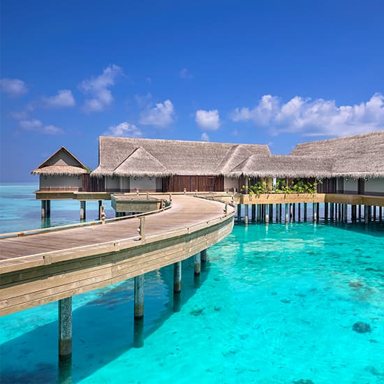 Luxurious overwater villa at luxury resort with private infinity pool overlooking turquoise Maldivian lagoon at sunset