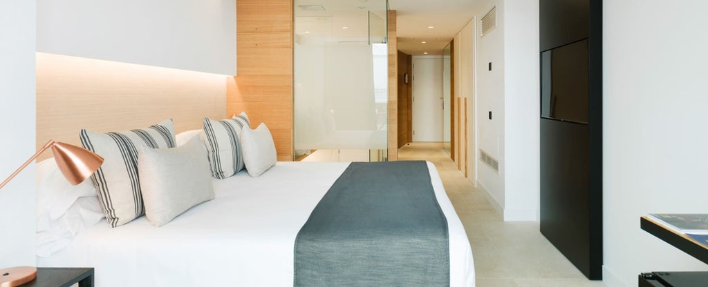 Modern, minimalist hotel room with sleek white furnishings, plush bed, and large window offering bright, airy atmosphere at a luxury boutique hotel in Spain.