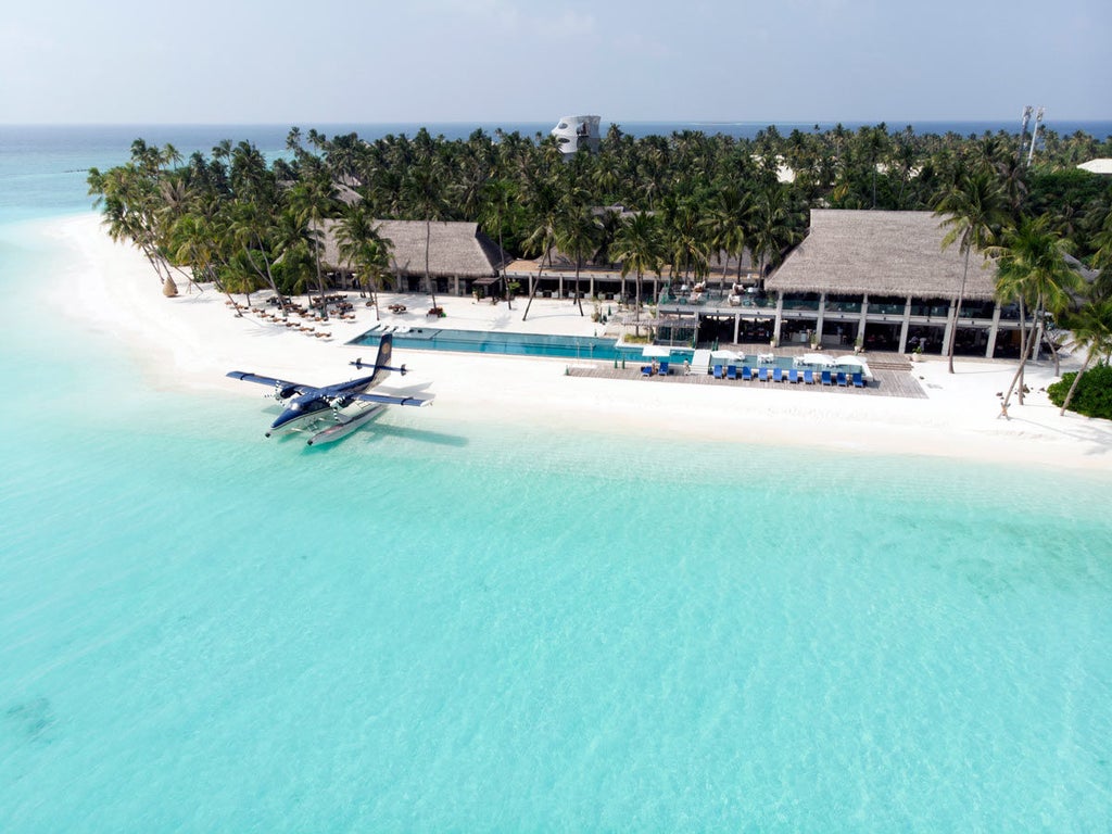 Luxurious overwater villa with private infinity pool overlooking turquoise Maldivian lagoon at sunset, wooden deck and steps to ocean