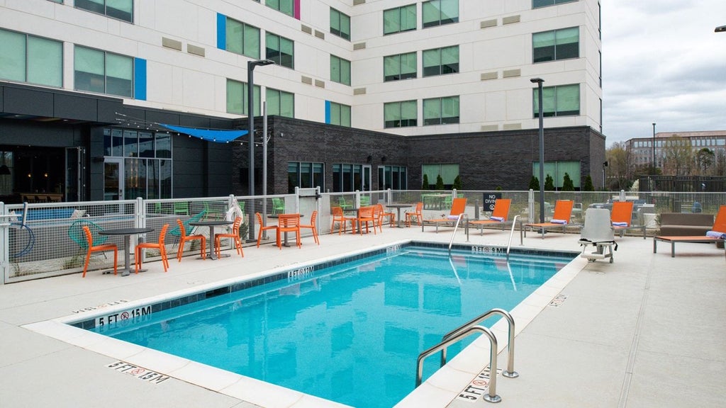 Modern, sleek hotel exterior with contemporary architectural design, glass facade, illuminated at dusk near airport with urban landscape backdrop.