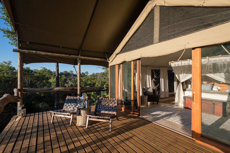 Elevated luxury safari tent with private deck overlooking pristine Okavango Delta floodplains, surrounded by lush greenery