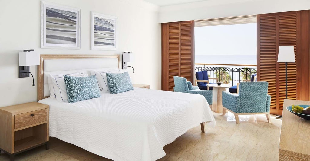 Luxurious sea view suite with elegant white furnishings, plush king bed, and panoramic azure Mediterranean vista at coastal Cyprus resort