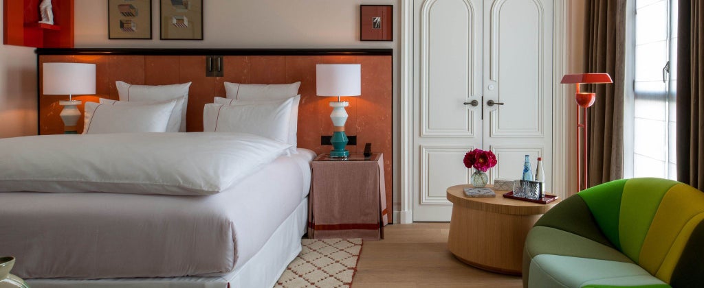 Elegant Deluxe hotel room with plush dark gray bedding, minimalist modern decor, and soft ambient lighting at Sinner Paris luxury accommodation