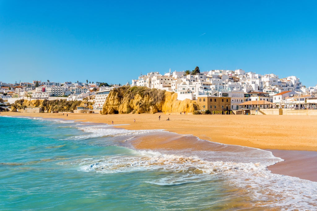 Sunlit luxury villa with infinity pool overlooking rugged Algarve coastline, featuring terracotta roofs and lush Mediterranean gardens