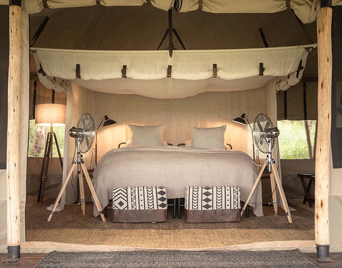 Elevated luxury safari tent with private deck overlooking Tanzania's wilderness at sunset, featuring canvas walls and teak furnishings