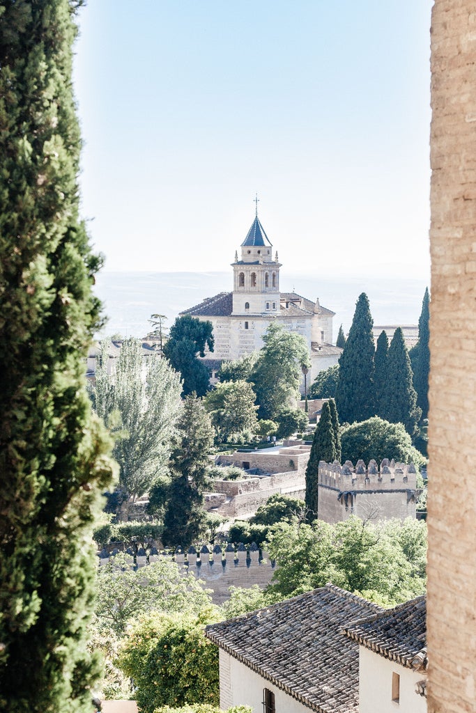 Granada's Alhambra palace viewed at sunset, with Sierra Nevada mountains in background, warm golden light illuminating ornate architecture