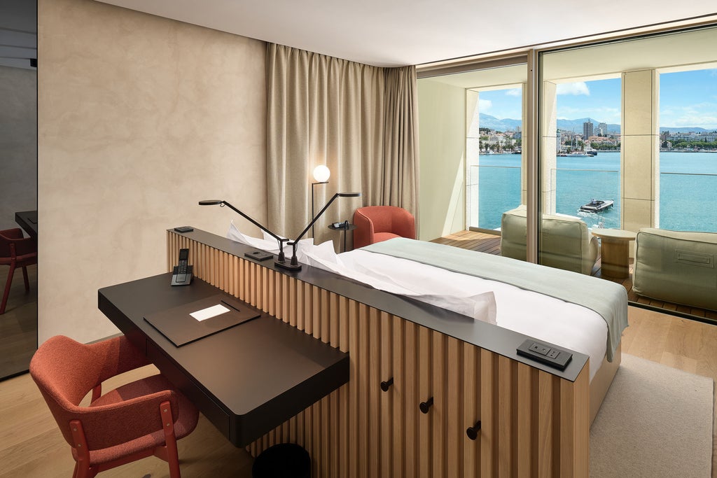 Luxurious hotel room featuring elegant wood furnishings, king-size bed with plush bedding, modern lighting, and panoramic Croatian sea views