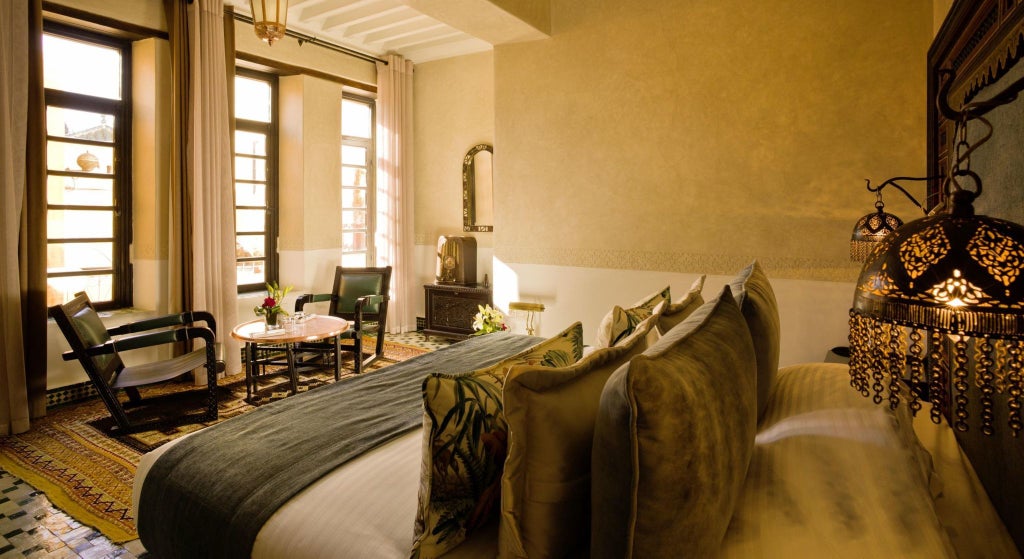 Elegant Moroccan-style classic hotel room with intricate blue and white tilework, ornate wooden furnishings, and traditional architectural details in Fès