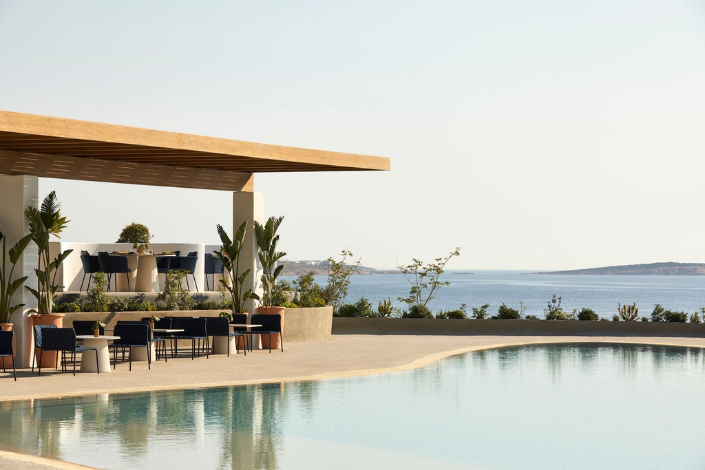 Elegant infinity pool overlooking Aegean Sea at sunset, with white marble terraces and Mediterranean architecture against cliffside