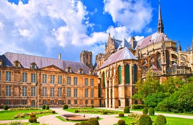 Gothic Reims Cathedral exterior with ornate twin towers, detailed carved portals and rose window, bathed in golden evening sunlight