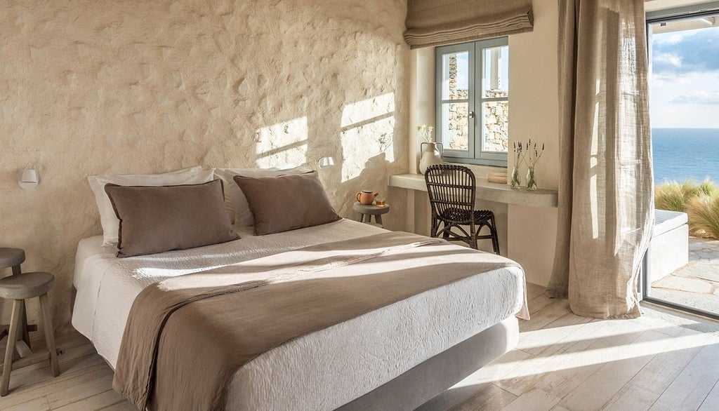 Minimalist white bedroom with expansive Aegean Sea view, featuring sleek design, crisp linens, and panoramic window at Verina Astra luxury boutique hotel in Sifnos, Greece.