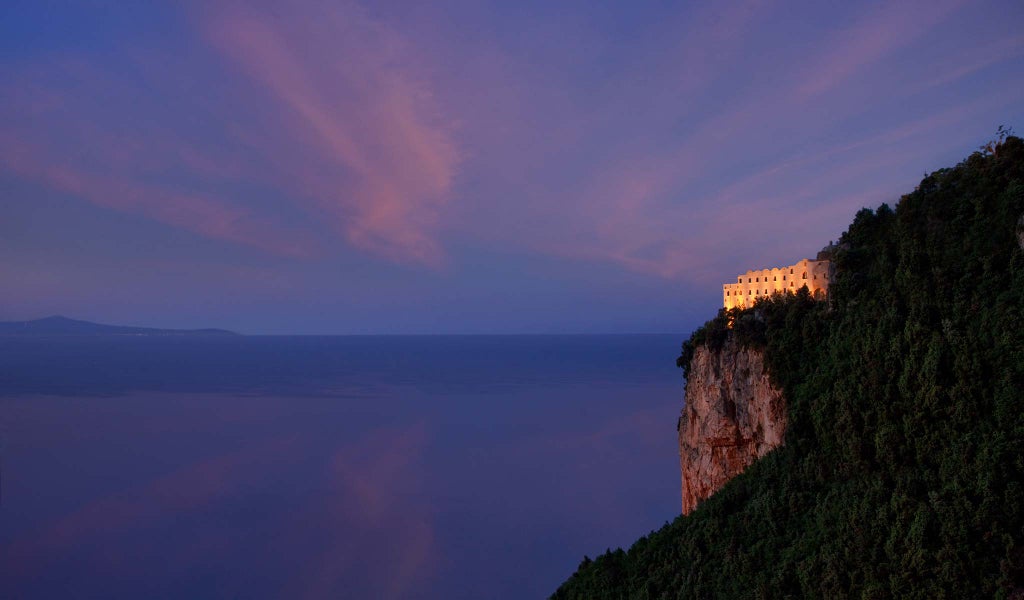 Historic Italian luxury hotel carved into cliffside with infinity pool overlooking Amalfi Coast's deep blue Mediterranean waters