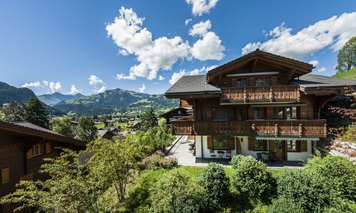 Elegant Swiss chalet-style suite with plush king bed, alpine wood paneling, ornate chandelier, and panoramic mountain view through large windows