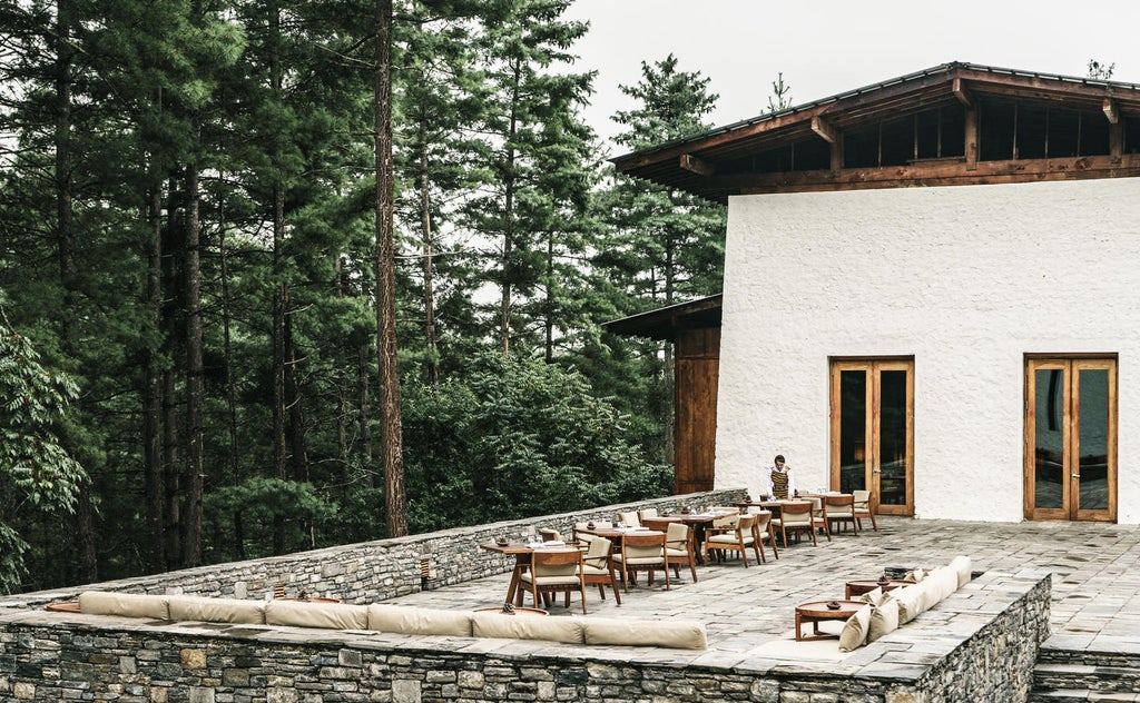 Luxurious mountain lodge with traditional Bhutanese architecture, nestled among pine forests with snow-capped Himalayan peaks backdrop