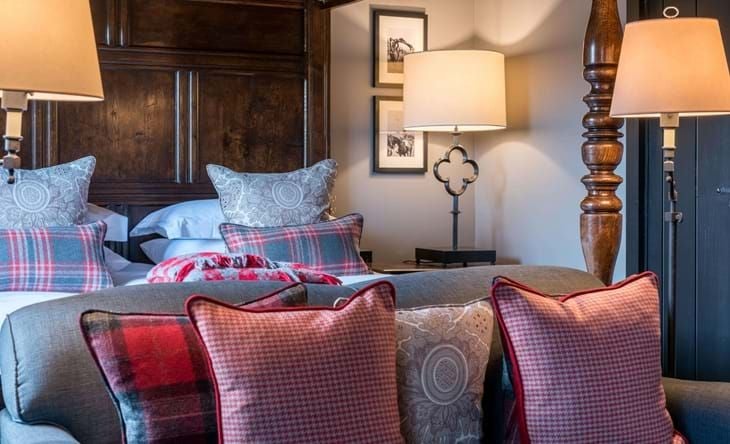 Four-poster bed with elegant cream linens, antique wooden furnishings, and traditional British countryside charm in a luxurious cottage suite at a historic hotel.