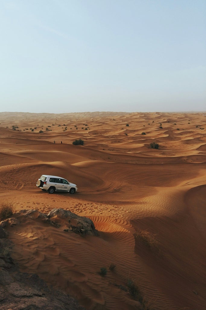 Luxurious desert SUV driving over golden sand dunes at sunset in Dubai, with traditional Arabic camp and adventurous off-road expedition landscape