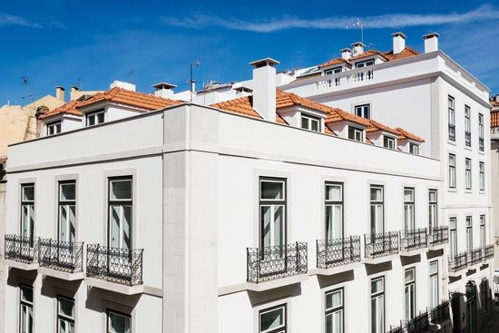 Luxurious white-walled boutique hotel suite in Lisbon with minimalist design, crisp linens, and large windows overlooking historic Portuguese architecture