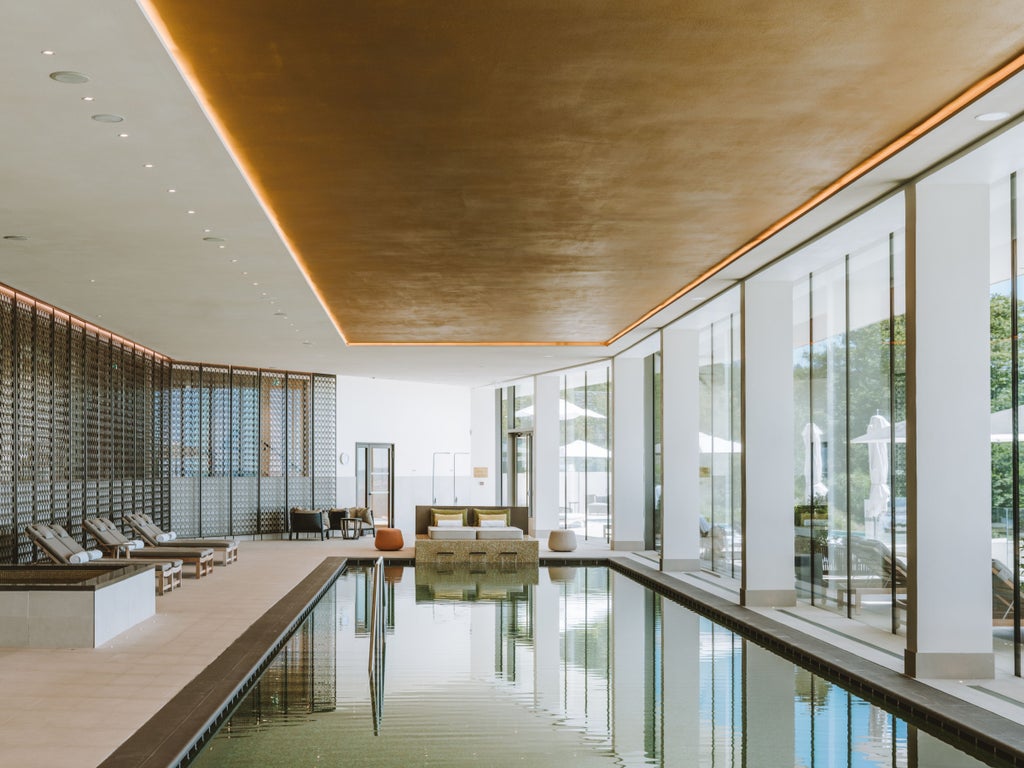 Elegant infinity pool overlooking rolling French vineyards at sunset, with modern lounge chairs and champagne-colored stone facade