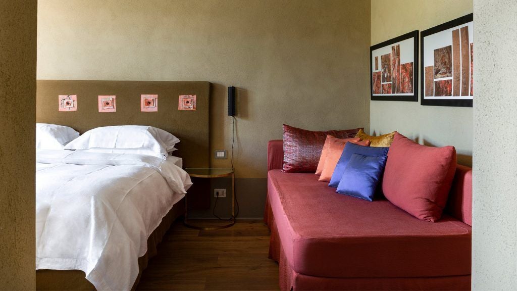 Elegant Tuscan-style hotel room with minimalist design, white linens, wooden floors, and panoramic window overlooking scenic Italian countryside landscape