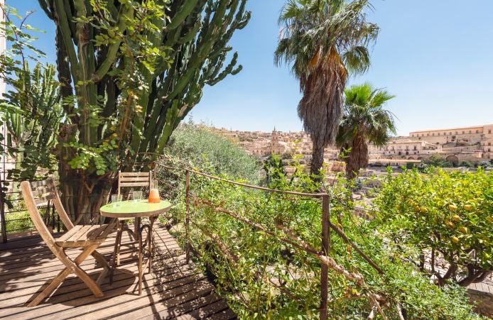 Elegant rustic Italian hotel room with warm terracotta tones, exposed stone walls, and handcrafted wooden furnishings overlooking Mediterranean landscape