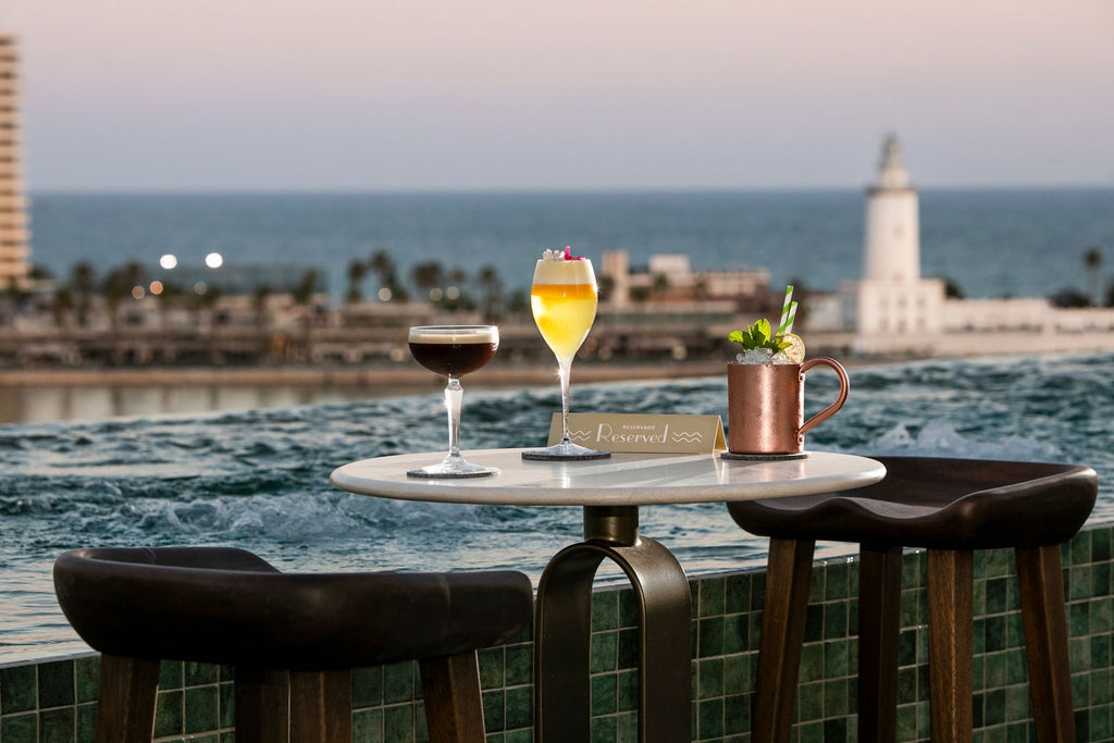 Elegant rooftop terrace of Only You Hotel with infinity pool overlooking Malaga's historic skyline and Mediterranean Sea at sunset.