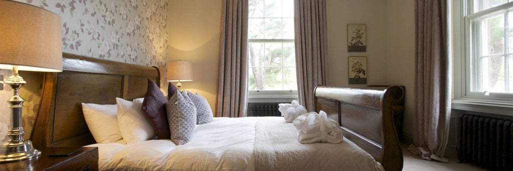 Luxurious bedroom at Yorebridge House hotel, featuring plush white bedding, elegant wooden furnishings, and large windows overlooking scenic landscape in Bainbridge, United Kingdom