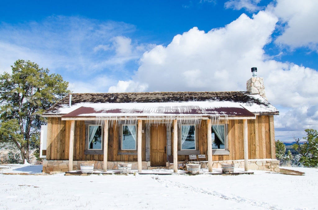 Rustic luxury lodge nestled against stunning mountain landscape, with wooden cabins, expansive deck, and panoramic scenset views of rugged wilderness terrain