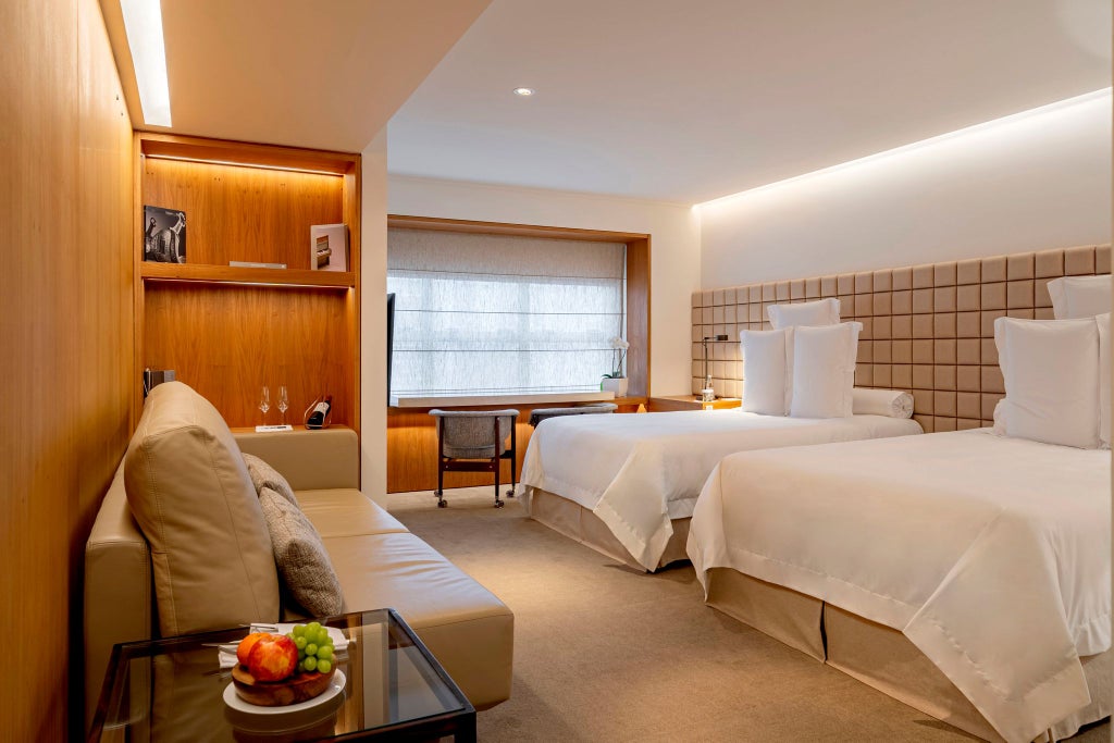 Luxurious hotel room with two sleek twin beds, minimalist decor, soft neutral tones, and expansive city view in São Paulo's upscale Hotel Emiliano