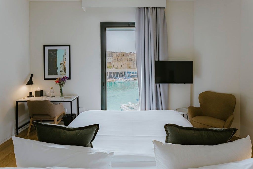 Elegant stone-walled luxury suite with minimalist designer furniture, high ceilings, and panoramic windows overlooking historic Maltese architecture in Senglea