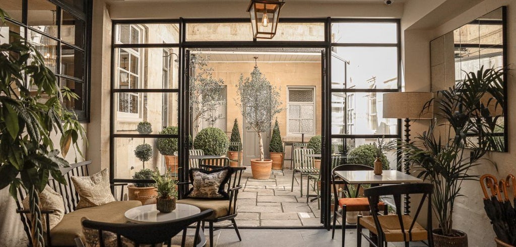 Elegant boutique hotel courtyard with modern design, featuring sleek outdoor furniture, soft lighting, and historic Bath stone architecture at dusk