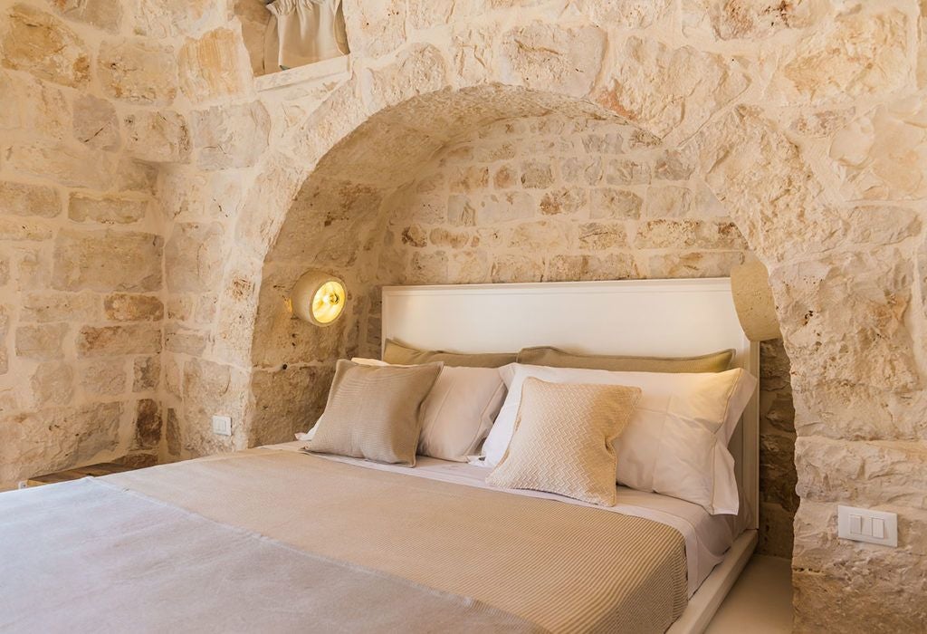 Luxurious stone Trullo suite at Borgo Canonica with traditional white-washed conical roof, rustic wooden furnishings, and elegant Mediterranean decor.